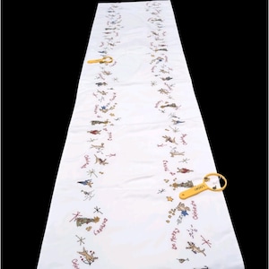 May include: A long white table runner featuring repeating festive illustrations of reindeer, stars, and champagne glasses, with the text "Celebrate" and "Be Merry" printed in red. Two yellow plastic magnifying glasses are placed on the fabric.
