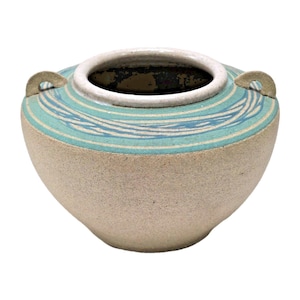 May include: A round ceramic pot with a textured beige body and a wide, smooth white rim. The upper section features a band of teal glaze decorated with swirling blue lines. Two small, arched handles are attached to opposite sides of the rim.