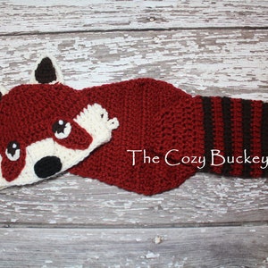 May include: Red and black crocheted baby hat and matching booties with a red panda face on the hat. The Cozy Buckeye is written on the booties.