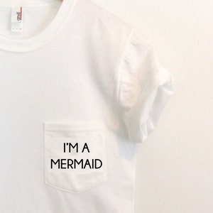 May include: White t-shirt with a pocket that says "I'm a Mermaid" in black text.