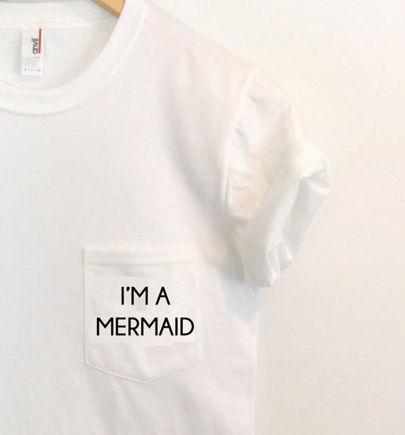 May include: White t-shirt with a pocket that says "I'm a Mermaid" in black text.
