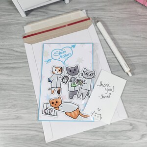 May include: A white envelope with a clear plastic sleeve containing a card with cartoon cats in lab coats. The card has the text "Storm Morgan" and "Thank you! -Storm!" written on it. A white pen is also included.