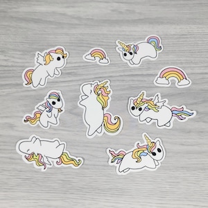 May include: A collection of white unicorn stickers with colorful manes and tails, along with two rainbow stickers. The unicorns are in various poses, some with wings. The stickers have a black outline.