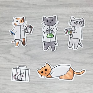 May include: A collection of cat stickers in lab coats, depicting various scientific activities. One cat holds a clipboard and pen, another a flask with green liquid, and a third holds test tubes. A cat is lying down, and another sticker shows a cat and a mouse in a cage.
