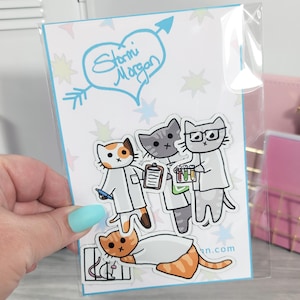 May include: A sticker sheet featuring cartoon cats dressed as scientists. The cats are in lab coats and holding beakers and clipboards. The top of the sheet has a blue heart with the words "Stormi Morgan" inside. The background is white with colorful stars.