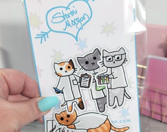 May include: A sticker sheet featuring cartoon cats dressed as scientists. The cats are in lab coats and holding beakers and clipboards. The top of the sheet has a blue heart with the words "Stormi Morgan" inside. The background is white with colorful stars.