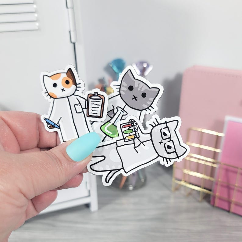 May include: Three cartoon cat stickers in lab coats. One cat holds a clipboard and pen, another a beaker, and the third a test tube rack. The cats have different fur patterns and wear glasses.
