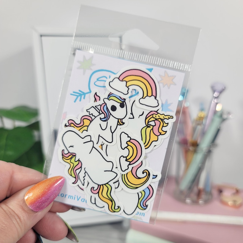 May include: A clear plastic package containing a set of unicorn stickers. The stickers feature white unicorns with colorful manes and tails, rainbows, and stars. The stickers are on a white background with blue and yellow accents. The text "ormiva" is visible.