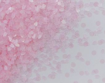 May include: Pink iridescent glitter in the shape of small leaves. The glitter is scattered on a white background.