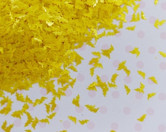 May include: A collection of small, bright yellow lightning bolt-shaped sequins. The individual pieces are metallic and reflective, scattered across a surface. These tiny, flat, die-cut shapes are uniform in color and design, creating a vibrant display.