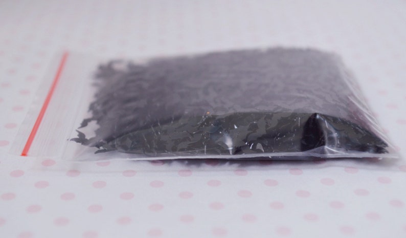 May include: A clear plastic bag with a red zipper closure filled with black confetti shaped like bats.