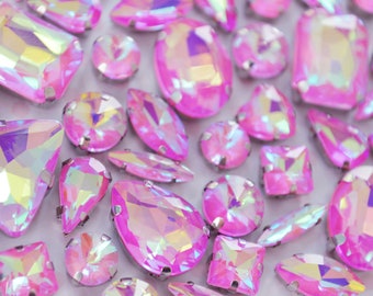 May include: A collection of faceted hot pink rhinestones in various shapes including ovals, rectangles, triangles, and teardrops. Each gemstone features an iridescent finish that reflects light, and they are set in silver-toned metal prongs.