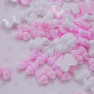 May include: A collection of pink and white plastic bows and flowers. The bows and flowers are scattered on a white background with pink polka dots.