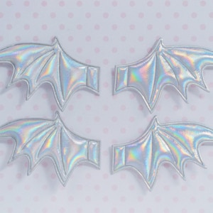 May include: Four iridescent silver bat wings with a pointed tip and a textured surface. The wings are arranged in pairs, with the tips of the wings pointing towards the center of the image.