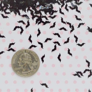May include: Black bat confetti scattered on a white background with pink polka dots. A US quarter is included for scale.