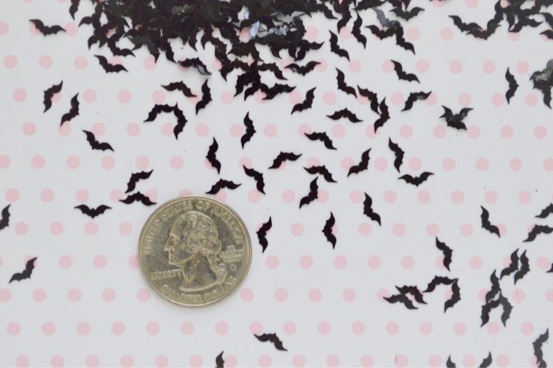 May include: Black bat confetti scattered on a white background with pink polka dots. A US quarter is included for scale.