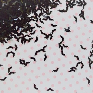 May include: Black bat-shaped glitter confetti scattered on a white background with pink polka dots.