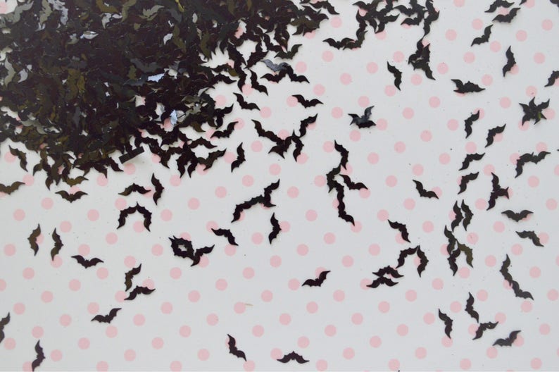 May include: Black bat-shaped glitter confetti scattered on a white background with pink polka dots.