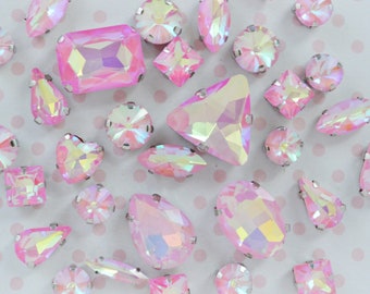 May include: Assortment of iridescent pink rhinestones in various shapes and sizes, including round, oval, teardrop, heart, square, and rectangular.