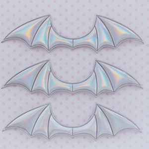 May include: Three pairs of iridescent silver bat wings, arranged in a vertical stack on a pink polka dot background.