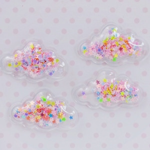 May include: Four clear cloud-shaped charms filled with colorful star-shaped confetti. The confetti includes shades of pink, yellow, green, and purple. The charms are on a light pink background with small white polka dots.