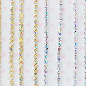 May include: Multiple vertical strands of rhinestone chain featuring iridescent, multi-colored crystals. The chains are set in either gold-toned or silver-toned metal settings, creating a linear arrangement of sparkling, reflective circular stones.