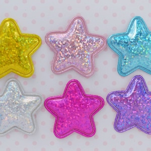 May include: Six star-shaped embellishments in various colors: yellow, pink, blue, silver, magenta, and purple. Each star has a glittery, iridescent center and a contrasting border. The stars are likely for crafts or decorations.