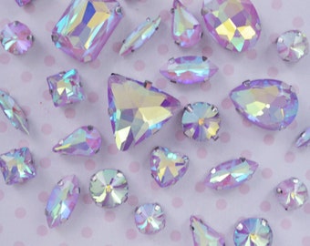 May include: Assortment of iridescent purple rhinestones in various shapes and sizes, including round, oval, teardrop, square, and triangular.