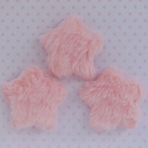 May include: Three pink fuzzy star-shaped embellishments. The stars are made of a soft, plush fabric.
