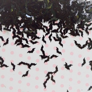 May include: Black glitter bat confetti. The bats are scattered on a white background with pink polka dots.