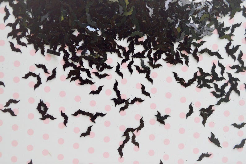 May include: Black glitter bat confetti. The bats are scattered on a white background with pink polka dots.