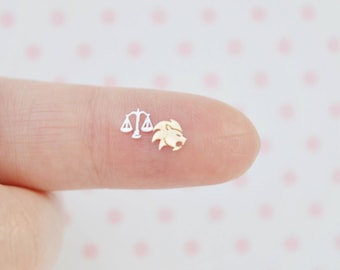 May include: Two small stud earrings, one silver-toned piece shaped like a scale of justice and one gold-toned piece shaped like a lion head. These tiny metal accessories are designed to be worn on the earlobe as a pair of mismatched zodiac symbols.