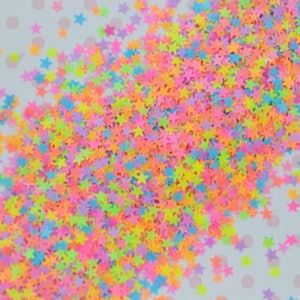 May include: A scattering of neon-colored star-shaped glitter on a white background with pink polka dots.