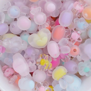 May include: A collection of pastel-colored plastic beads in various shapes, including hearts, flowers, and bunnies. The beads are translucent and have a frosted finish.