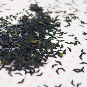May include: Black glitter bat confetti scattered on a white background with pink polka dots.