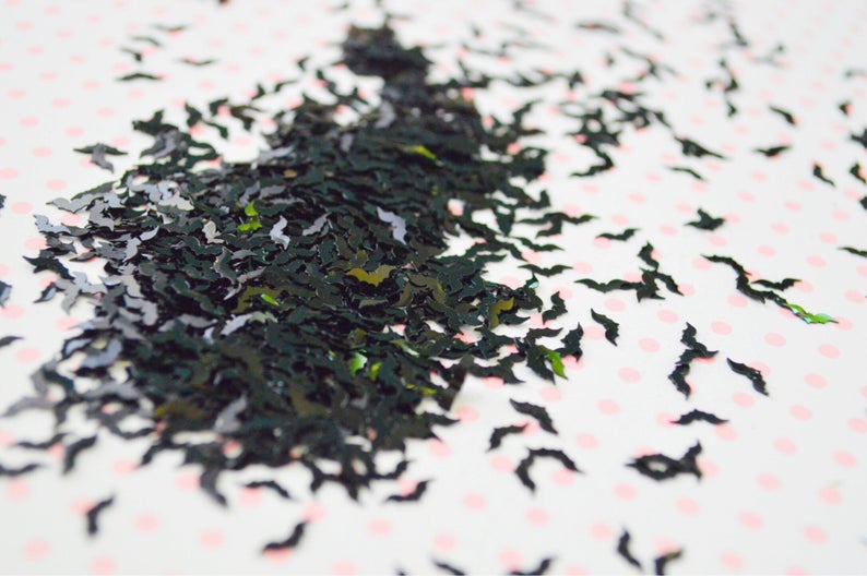 May include: Black glitter bat confetti scattered on a white background with pink polka dots.
