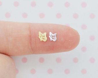 May include: Two miniature butterfly-shaped charms, one in a gold tone and one in a silver tone. Each charm features a delicate, open-work filigree design with intricate cutouts representing the wings of a butterfly, displayed side by side.