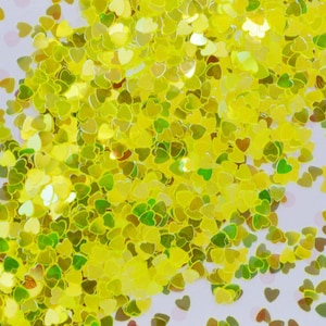 May include: A large quantity of yellow heart-shaped glitter. The glitter is iridescent and has a holographic finish.