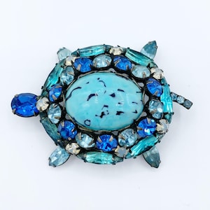 May include: A turquoise and blue jeweled turtle brooch. The turtle's shell is made of a turquoise cabochon surrounded by blue and turquoise rhinestones.