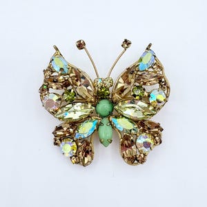 May include: A gold tone butterfly brooch with iridescent clear and brown rhinestones and a green cabochon center.