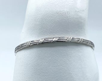 Könnte beinhalten: Ein silbernes Armreif-Armband mit einem dekorativen Design aus ineinander verschlungenen Linien und kleinen Punkten.