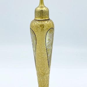 May include: A gold-colored glass perfume bottle with a textured surface and a clear glass base. The bottle has a decorative design and a gold-colored metal spray nozzle.