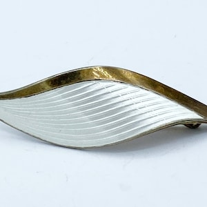 Peut inclure: Une broche en forme de feuille en émail blanc et or. La broche a une surface en émail blanc texturé avec une bordure dorée.
