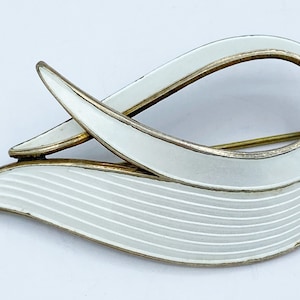 Peut inclure: Une broche en argent sterling et émail blanc avec un design abstrait et fluide. La broche a une finition émail blanc délicatement peinte à la main et un cadre en métal argenté.