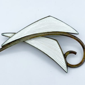 Peut inclure: Une broche en argent et émail blanc avec un motif géométrique. La broche est en forme de deux feuilles abstraites avec une tige incurvée.