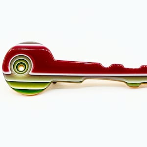 May include: A decorative key-shaped pin with a vibrant design. The pin features a red, green, and white striped pattern on the head and a red body. The key is set against a white background.
