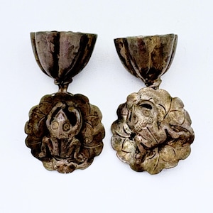May include: A pair of antique silver-toned earrings. Each earring features a detailed frog design on a floral base, connected to a cup-shaped top. The earrings have an aged, vintage appearance, with intricate detailing.