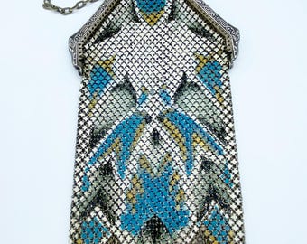 May include: A silver mesh purse with a blue, yellow, and white geometric pattern. The purse has a chain strap and a fringe bottom.
