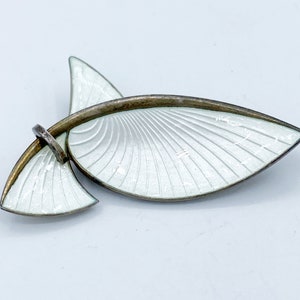 Peut inclure: Une broche en argent et émail blanc en forme de feuille stylisée. La broche a un design délicat et complexe avec une forme incurvée.