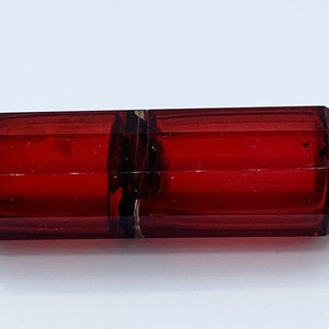 Puede incluir: Una botella de vidrio roja con tapas plateadas. La botella es facetada y tiene una forma rectangular.